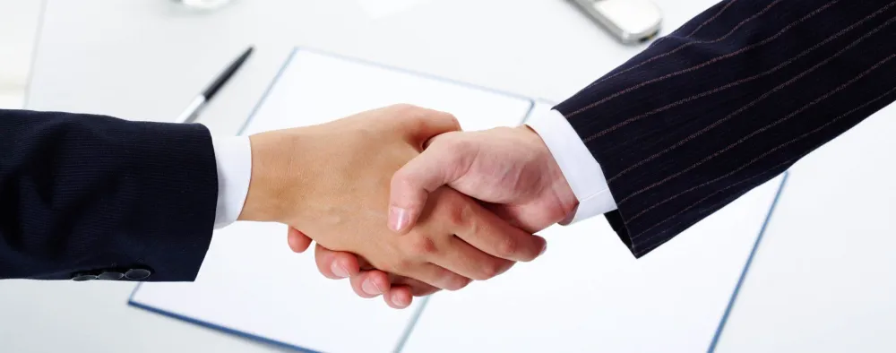 Two people shaking hands over a contract